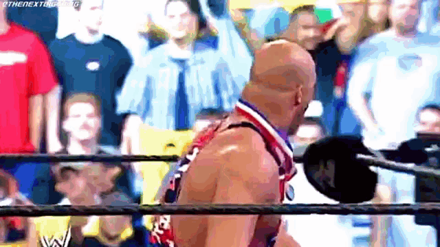 a bald man is standing in a wrestling ring in front of a crowd of people .