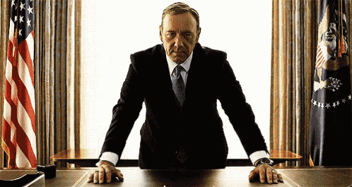 a man in a suit and tie is standing at a desk with his hands on the table