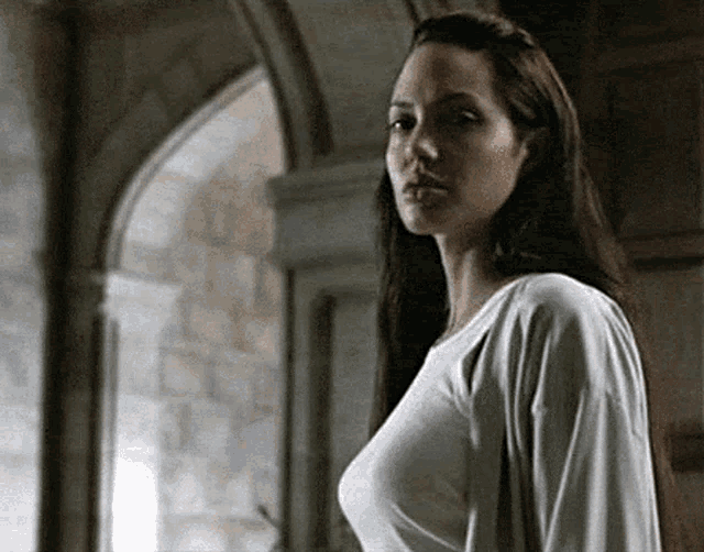 a woman with long hair and a white shirt is standing in front of a window .