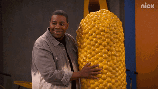 a man is holding a large corn on the cob in front of a nick sign