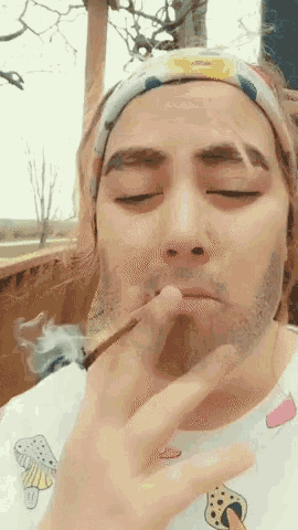 a man wearing a headband is smoking a cigarette with his eyes closed