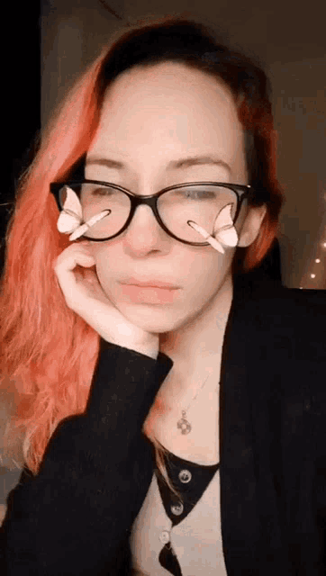 a woman with pink hair and glasses has a butterfly on her face .