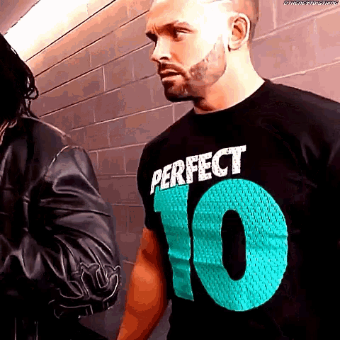 a man wearing a perfect 10 t-shirt stands in front of a brick wall