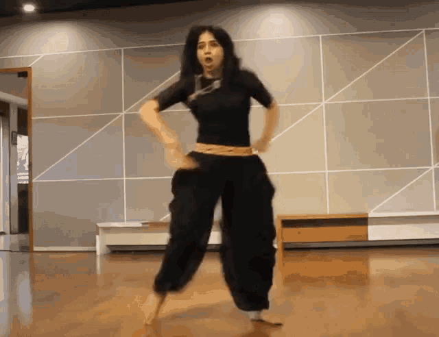 a woman in a black shirt and black pants is dancing in a room