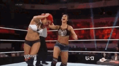two women are wrestling in a wrestling ring with a referee in the background .