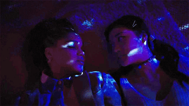 a couple of women are kissing in a dark room with purple lights .
