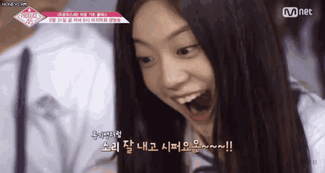a girl is smiling with her mouth open in front of a sign that says produce 48 on it