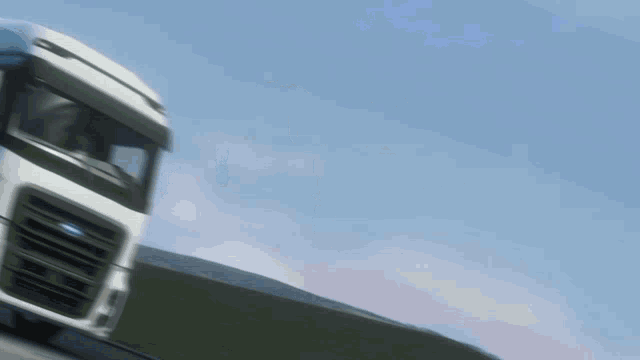 a white truck is driving down a road with a blue sky in the background