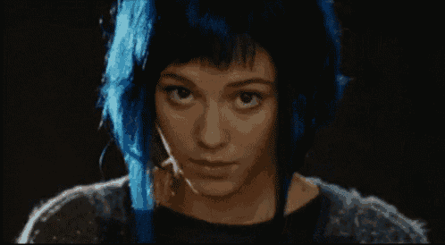 a woman with blue hair looks at the camera with a serious look on her face