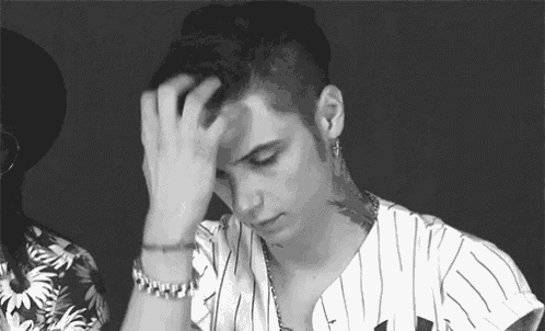 a man with a tattoo on his neck is holding his hand to his forehead .