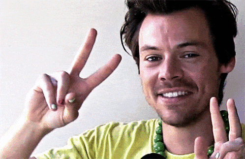 a man in a yellow shirt is smiling and giving a peace sign