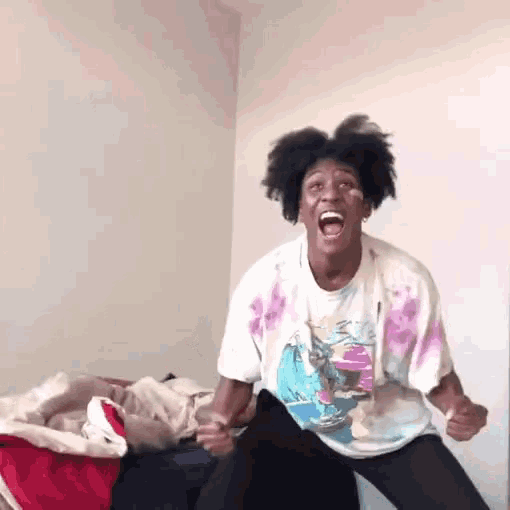 a man in a tie dye shirt is sitting on a bed with his mouth wide open
