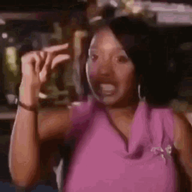 a woman in a pink shirt is making a funny face and pointing her finger .