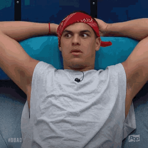 a man wearing a red bandana and a white tank top is laying on a blue couch .
