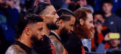a group of men with beards are standing next to each other in a row in front of a crowd .