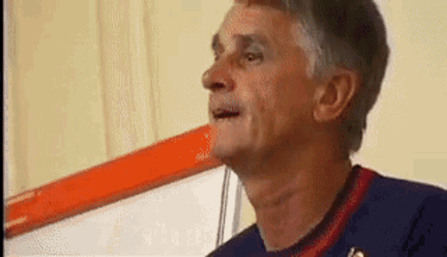 a man with gray hair is wearing a blue and red shirt and making a funny face .