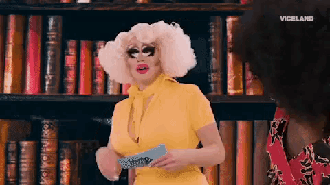 a drag queen is standing in front of a bookshelf with viceland written on the bottom right