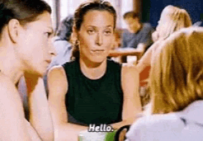 a group of women are sitting at a table talking to each other and one woman is saying hello .