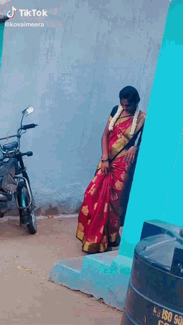 a woman in a red saree is standing next to a motorcycle on a street