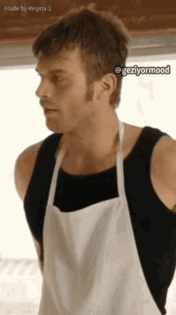 a man wearing an apron and a black tank top is standing in a kitchen .