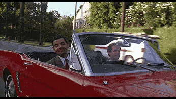 a man in a suit and tie is driving a red convertible car with another man in the back seat .