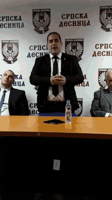 a man in a suit and tie is giving a speech in front of a wall that says " cpscka desnica " on it