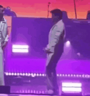 a man in a white suit is dancing on a stage with purple lights behind him .