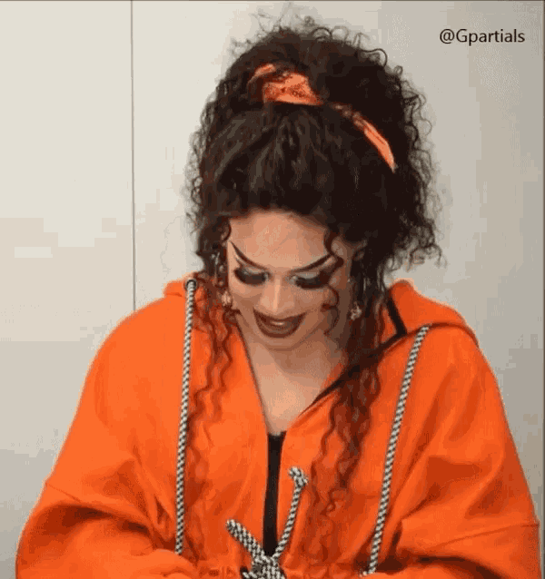 a woman with curly hair wearing an orange jacket and a bandana on her head .