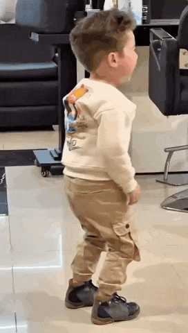 a little boy is standing in a room in a hair salon .