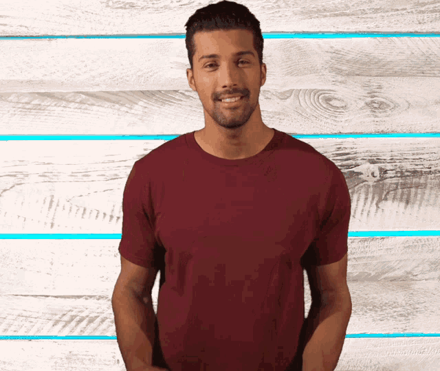a man wearing a maroon t-shirt is smiling in front of a wooden wall
