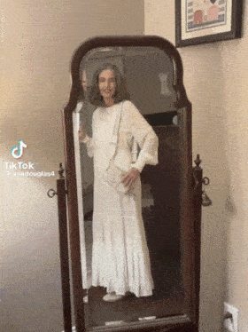 a woman in a white dress is standing in front of a mirror with tiktok written on the bottom