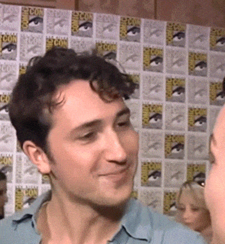 a man in a blue shirt is smiling in front of a wall with comic con posters on it .