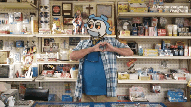 a man making a heart shape with his hands in front of a shelf full of items with #kimsconvenience reactions on the bottom