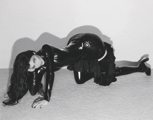 a black and white photo of a woman in a latex outfit on her knees