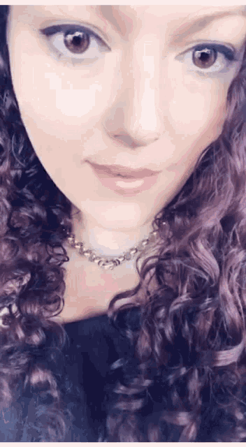 a close up of a woman 's face with purple hair and a gold necklace