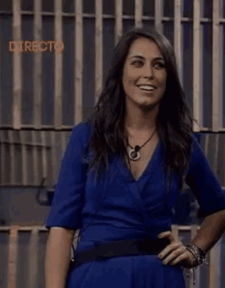 a woman in a blue dress is standing in front of a fence with the word directo on it