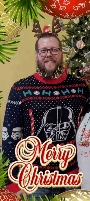 a man wearing a darth vader sweater stands in front of a merry christmas card