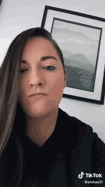 a woman in a black shirt is standing in front of a framed picture that says ' mountains ' on it