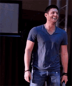 a man wearing a blue t-shirt and jeans is smiling and holding a microphone .
