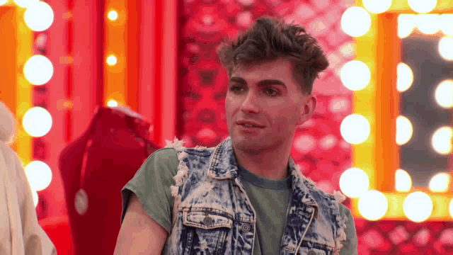 a man in a denim vest is standing in front of a red background