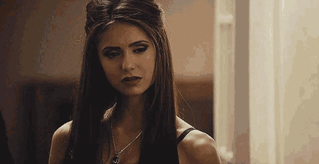a woman wearing a black top and a necklace is looking at the camera .