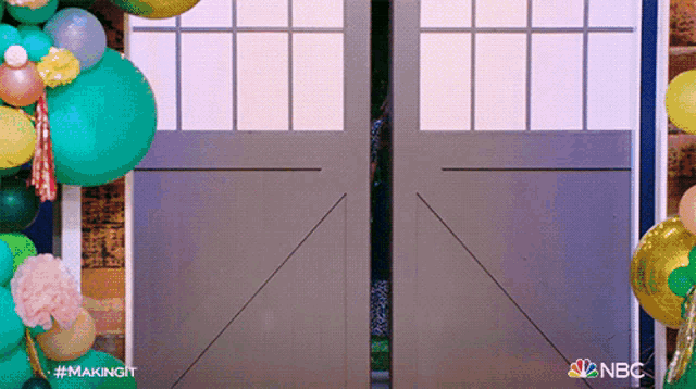 a nbc ad shows a person standing in front of a door surrounded by balloons .