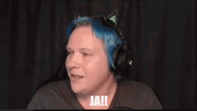 a man with blue hair and cat ears is wearing headphones and laughing with his hands in the air .
