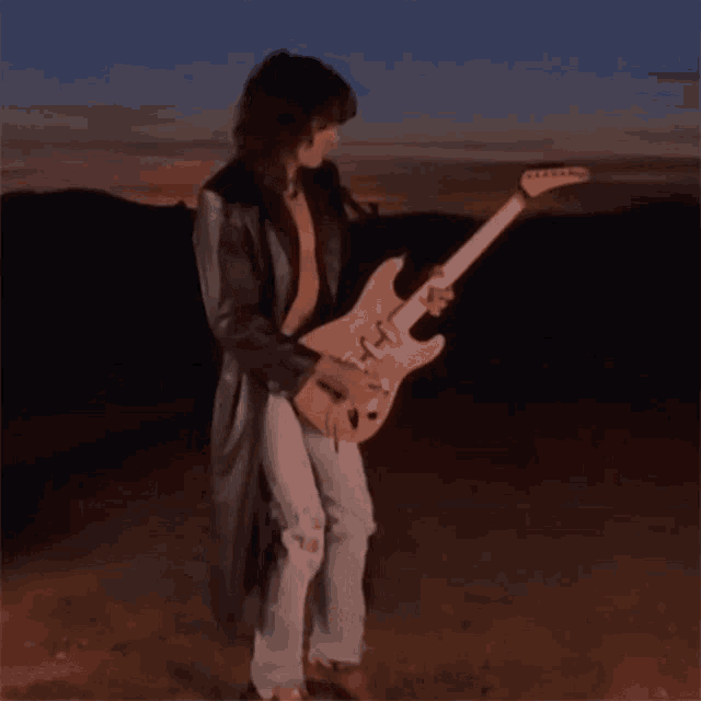 a man in a trench coat is playing a guitar in the desert
