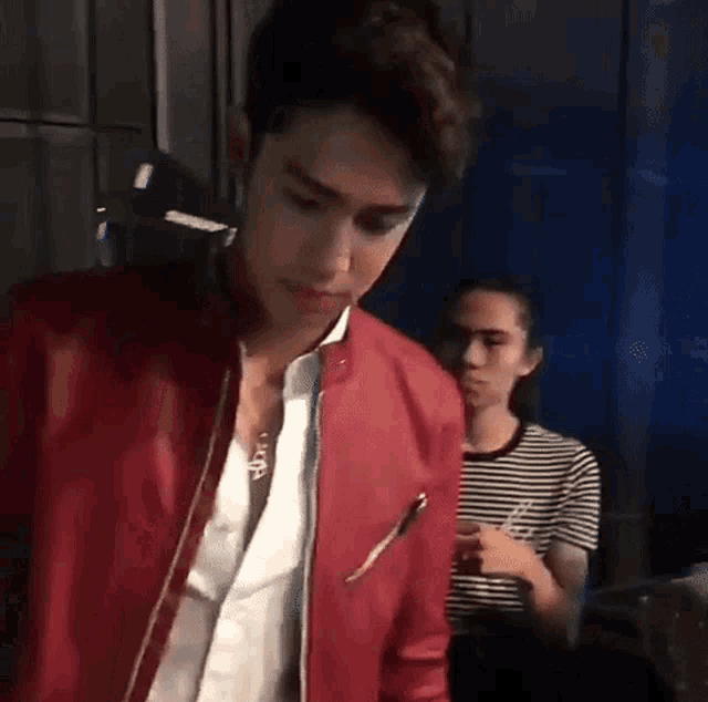 a man wearing a red leather jacket and a white shirt is standing next to a woman in a striped shirt .