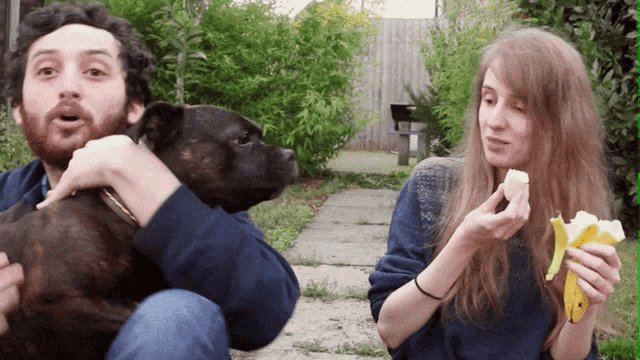 a man holds a dog while a woman peel a banana