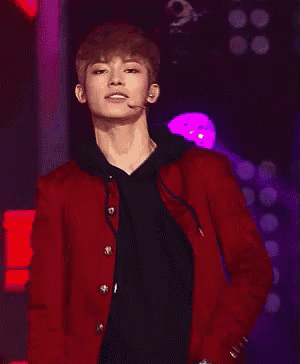 a young man in a red jacket is holding a microphone and smiling on a stage .