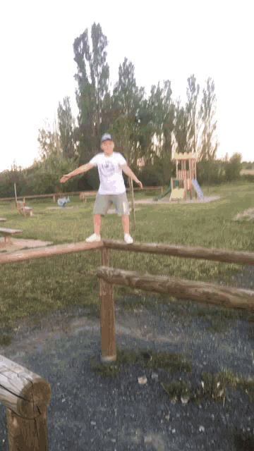 a young boy stands on a wooden fence in a park