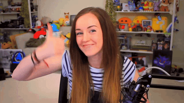 a girl in a striped shirt holds a microphone in front of a shelf full of stuffed animals