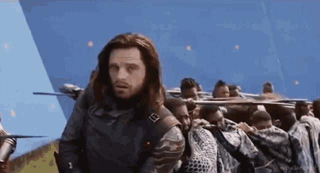 a man with long hair and a beard is standing in front of a group of people holding guns .